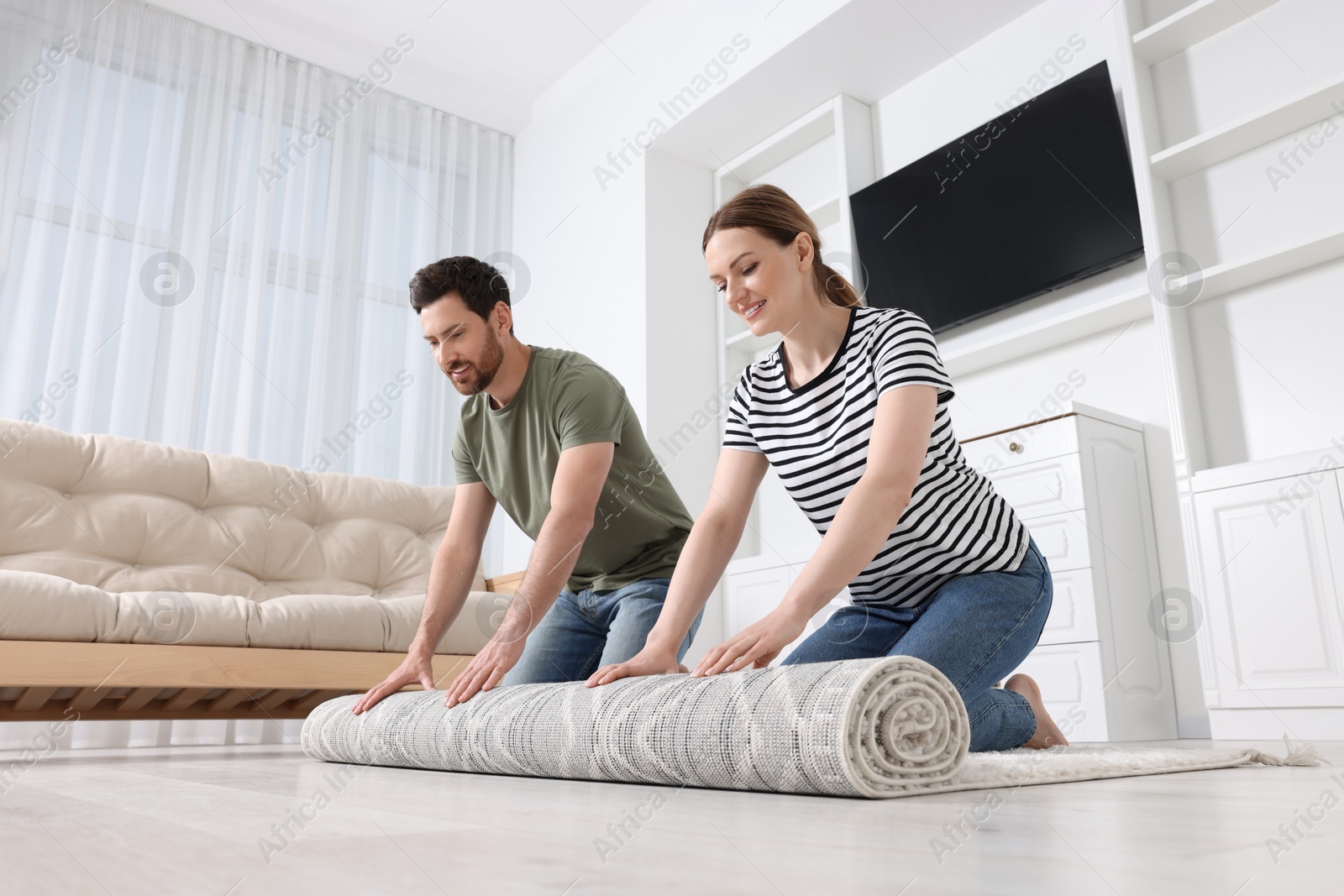 Photo of Smiling couple unrolling carpet with beautiful pattern on floor in room