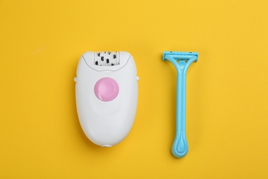 Modern epilator and shaving razor on yellow background, flat lay