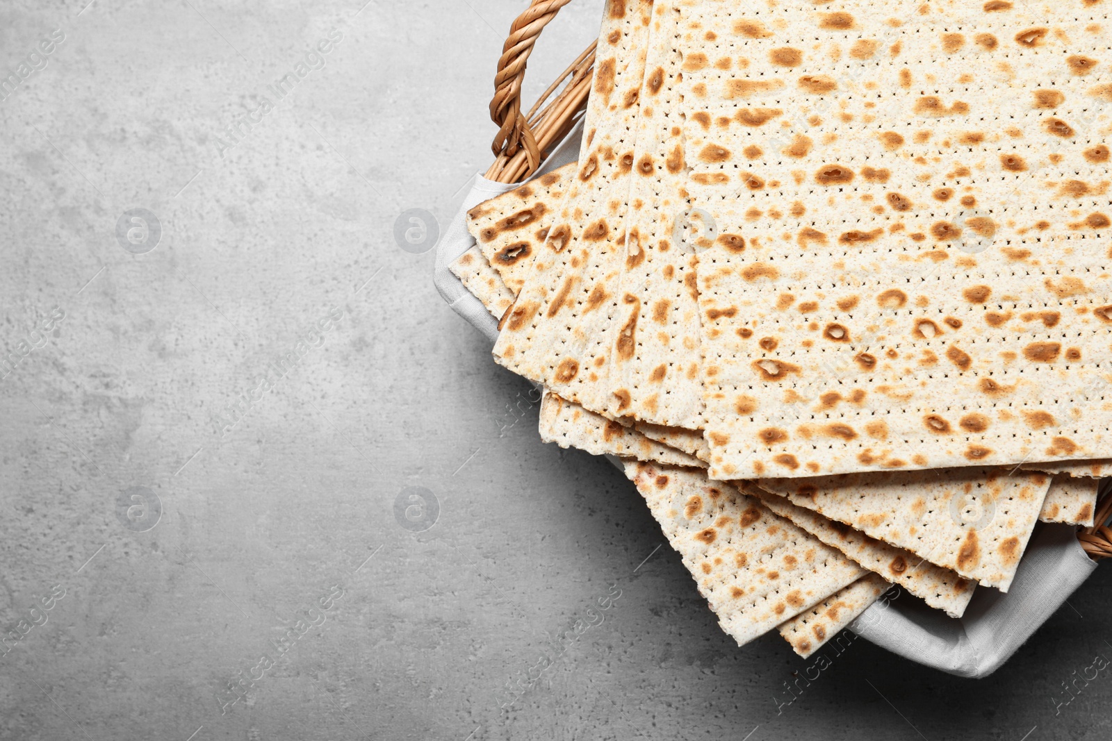 Photo of Traditional matzos in basket on light grey table, top view. Space for text