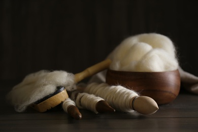 Photo of Soft white wool and spindles on wooden table, closeup