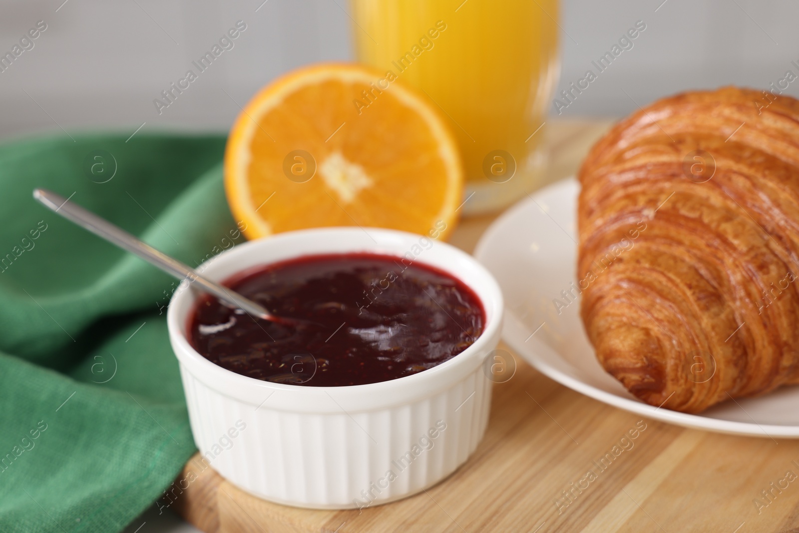 Photo of Breakfast time. Fresh croissant and jam on wooden board, closeup