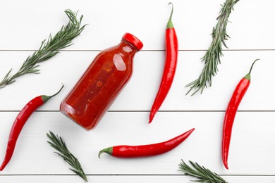 Photo of Spicy chili sauce in bottle, peppers and rosemary on white wooden table, flat lay