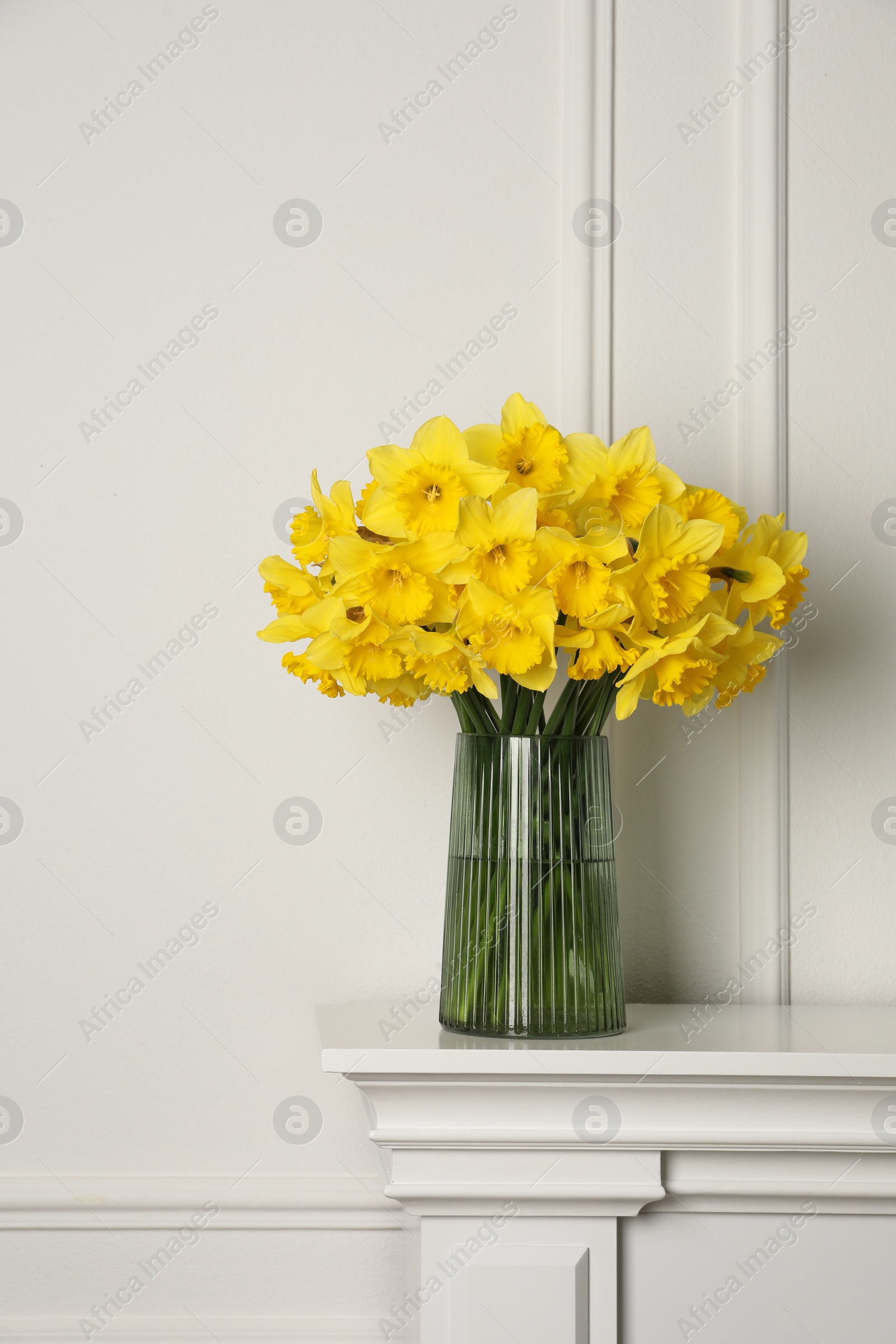 Photo of Beautiful daffodils in vase on table near white wall indoors