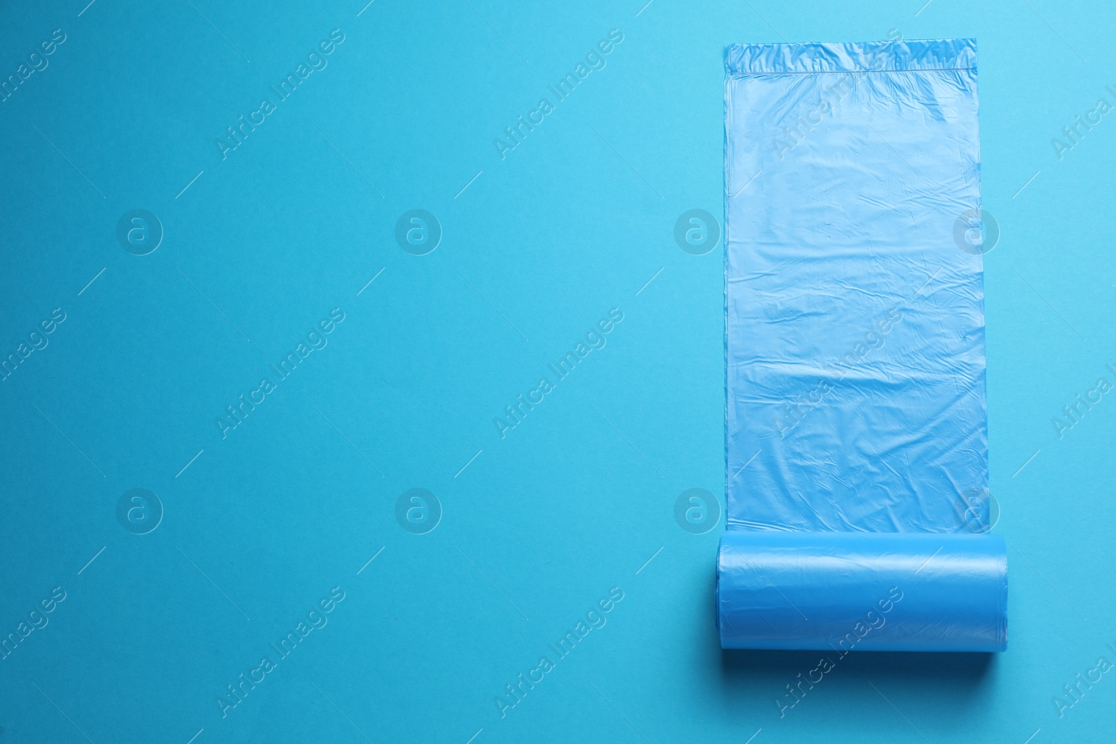 Photo of Roll of turquoise garbage bags on light blue background, top view. Space for text