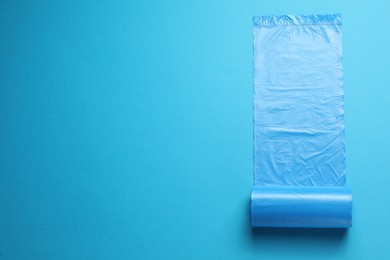 Photo of Roll of turquoise garbage bags on light blue background, top view. Space for text