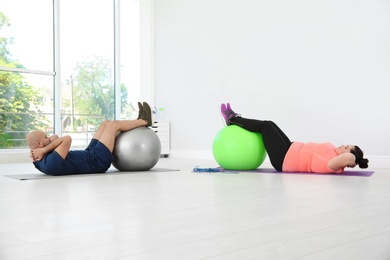 Overweight man and woman doing exercise with fitness balls in gym