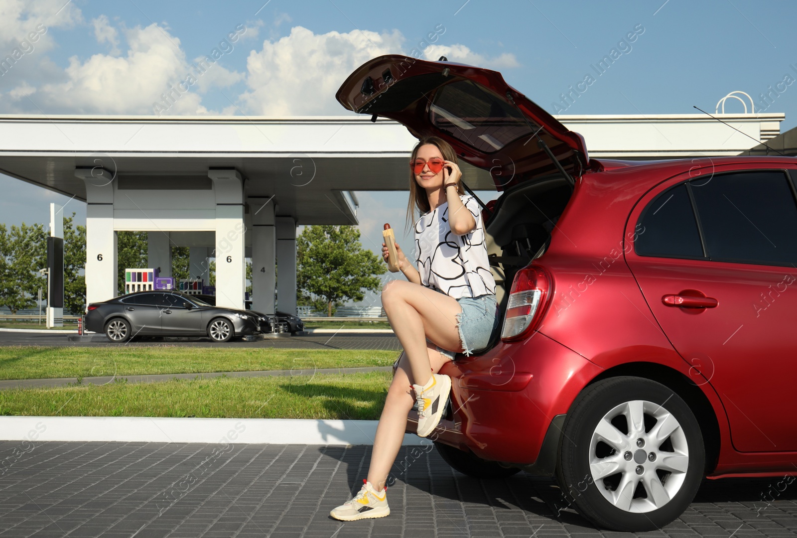 Photo of Beautiful young woman with hot dog near car at gas station