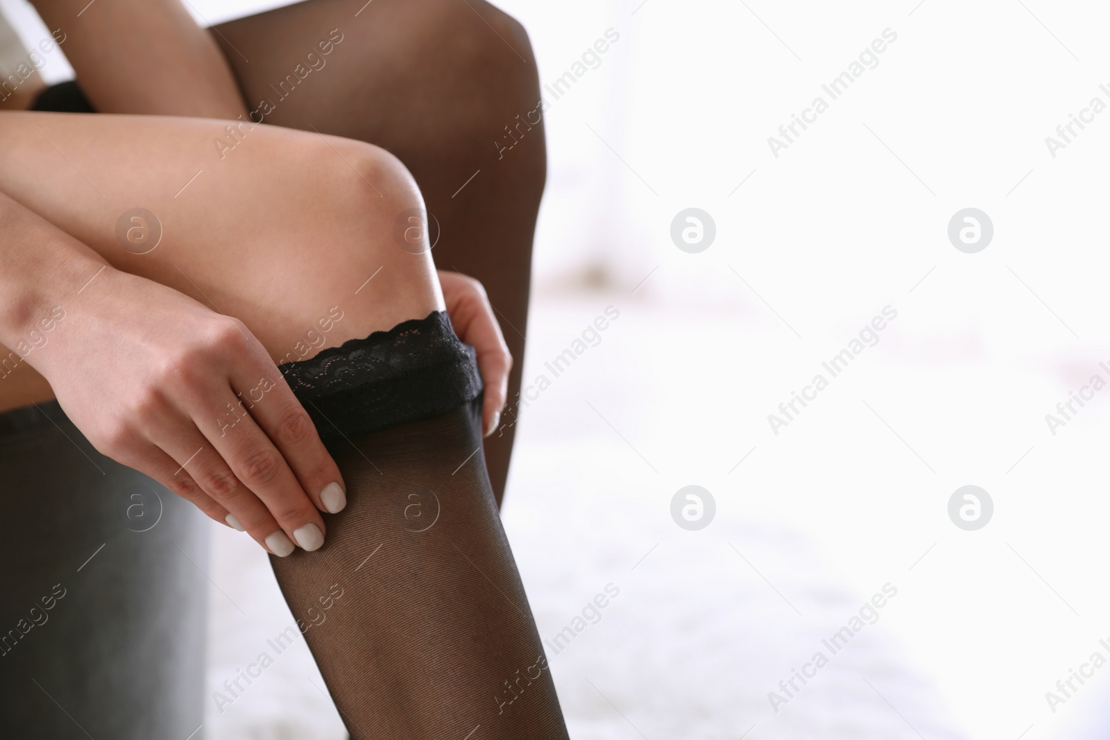 Photo of Beautiful woman putting on stocking indoors, closeup