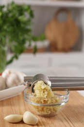 Photo of Garlic press, cloves and mince on wooden table in kitchen, closeup