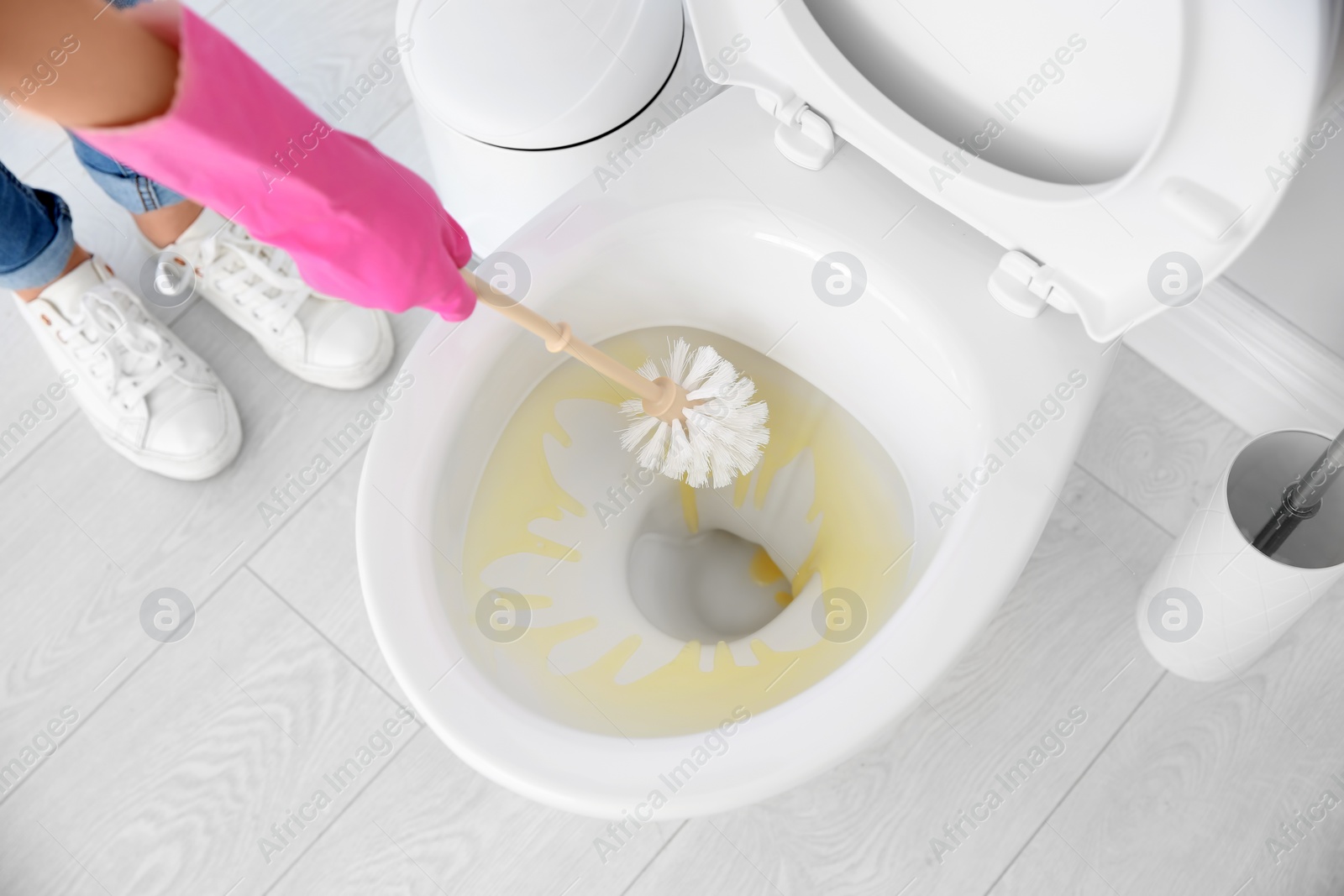 Photo of Woman cleaning toilet bowl in bathroom, closeup