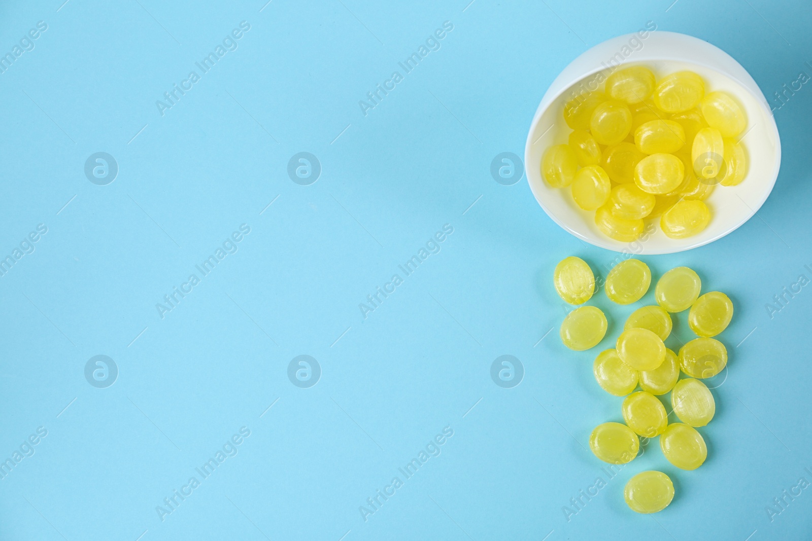 Photo of Delicious lemon drops and bowl on light blue background, flat lay. Space for text