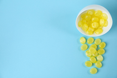 Photo of Delicious lemon drops and bowl on light blue background, flat lay. Space for text