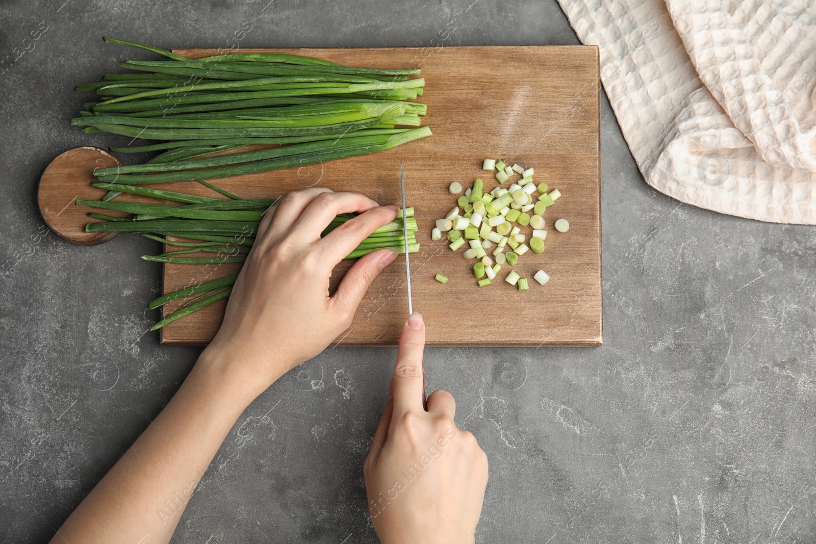 Photo of Woman cutting fresh green onion on wooden board, top view