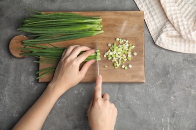 Photo of Woman cutting fresh green onion on wooden board, top view