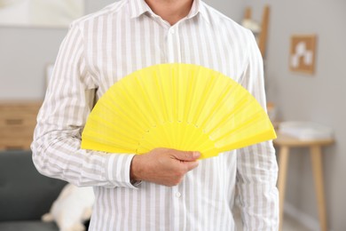 Man with yellow hand fan indoors, closeup