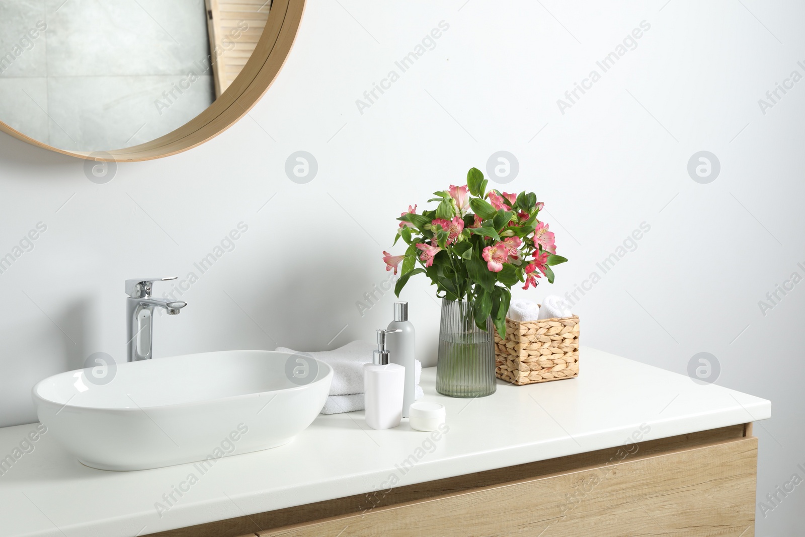 Photo of Vase with beautiful Alstroemeria flowers and toiletries near sink in bathroom