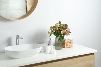 Vase with beautiful Alstroemeria flowers and toiletries near sink in bathroom