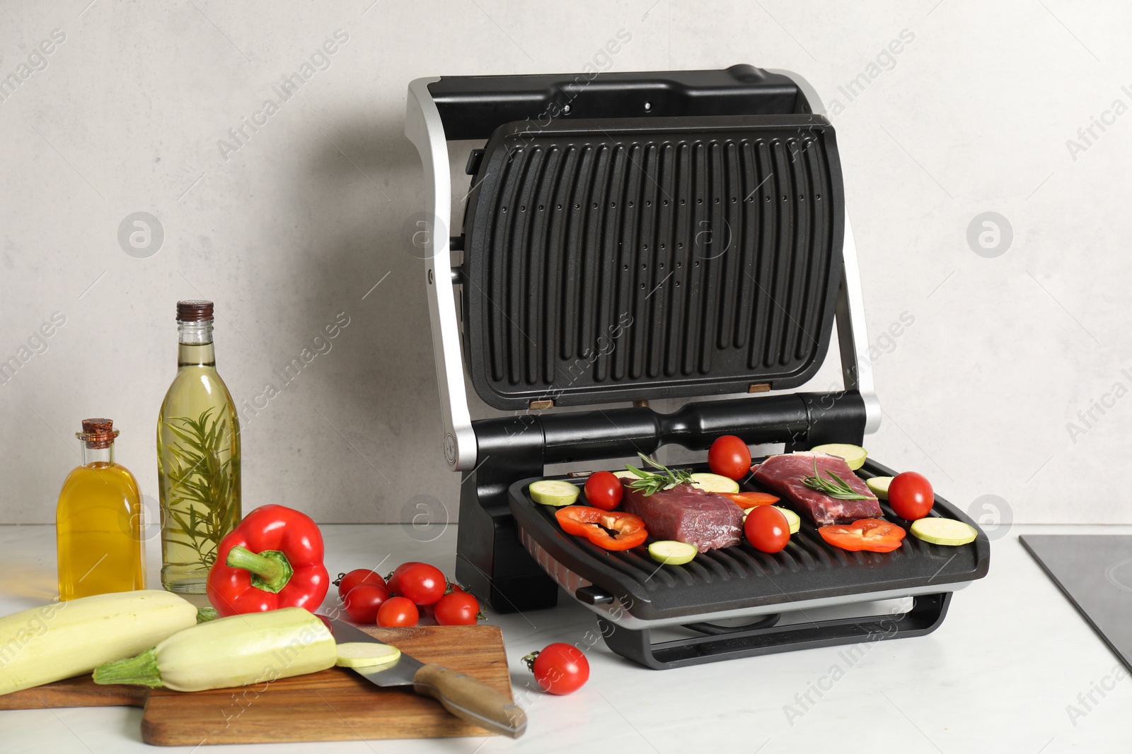 Photo of Electric grill and different products on white wooden table