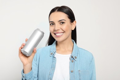 Beautiful happy woman holding beverage can on light grey background