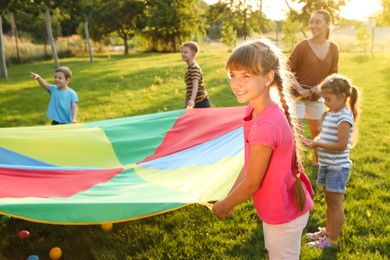 Photo of Group of children and teacher playing with rainbow playground parachute on green grass. Summer camp activity