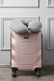 Photo of Striped travel pillow on suitcase near light wall indoors