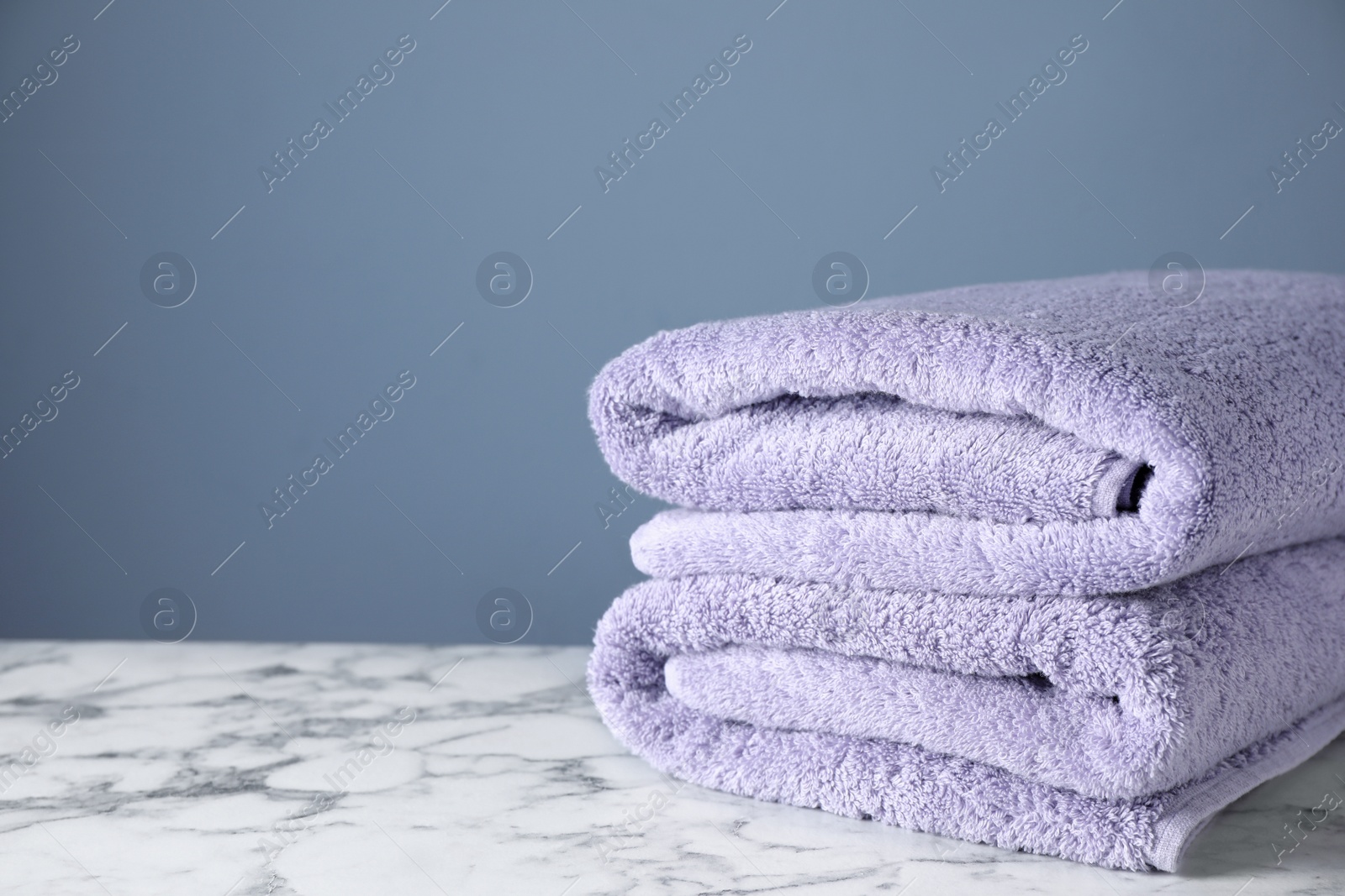 Photo of Stack of clean bath towels on white marble table. Space for text