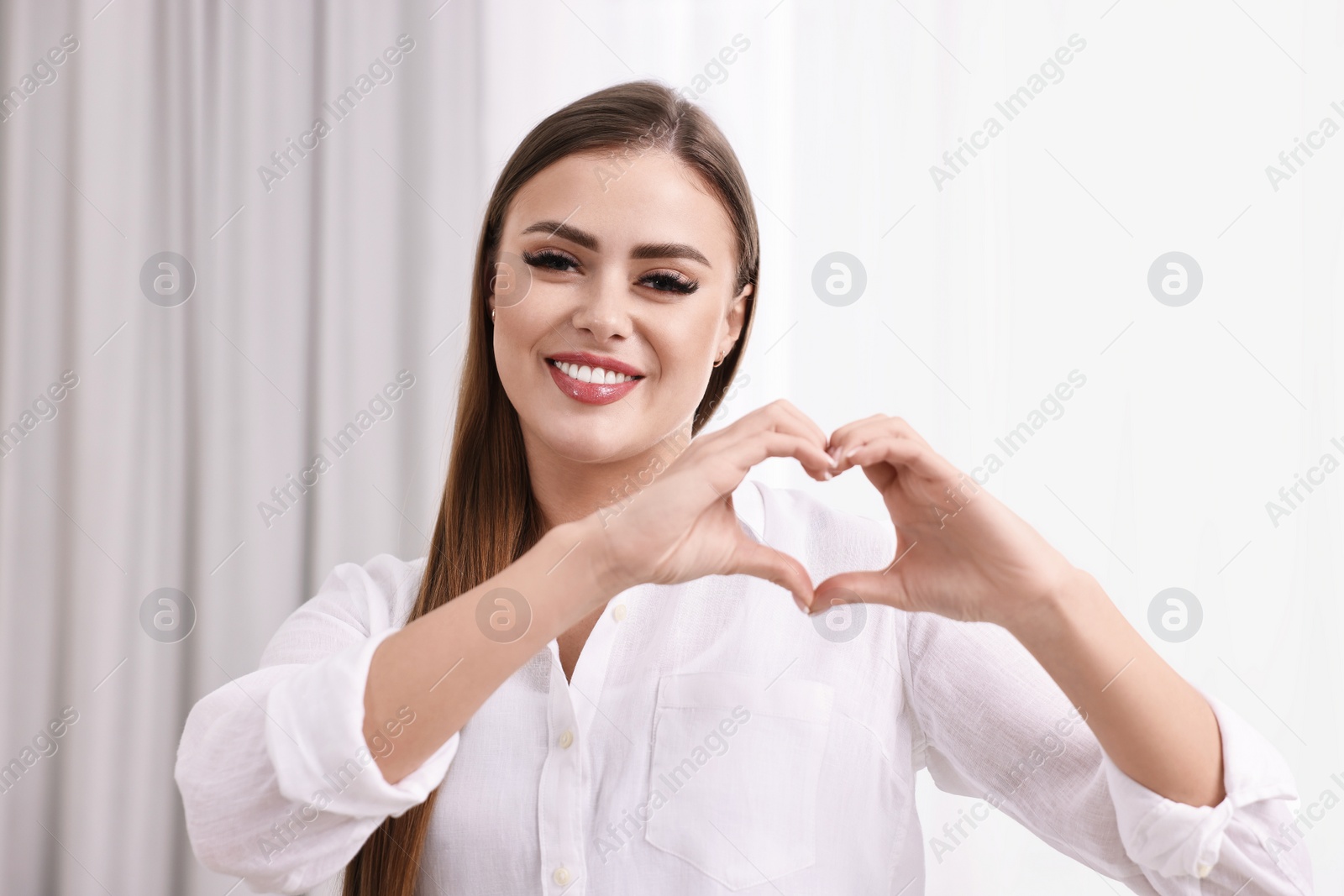 Photo of Happy woman showing heart gesture with hands indoors