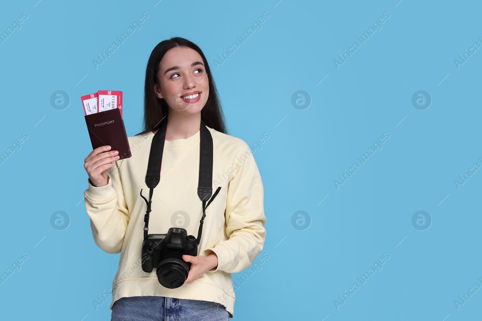 Photo of Happy woman with passport, tickets and camera on light blue background. Space for text