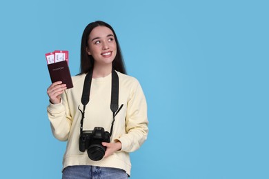 Happy woman with passport, tickets and camera on light blue background. Space for text