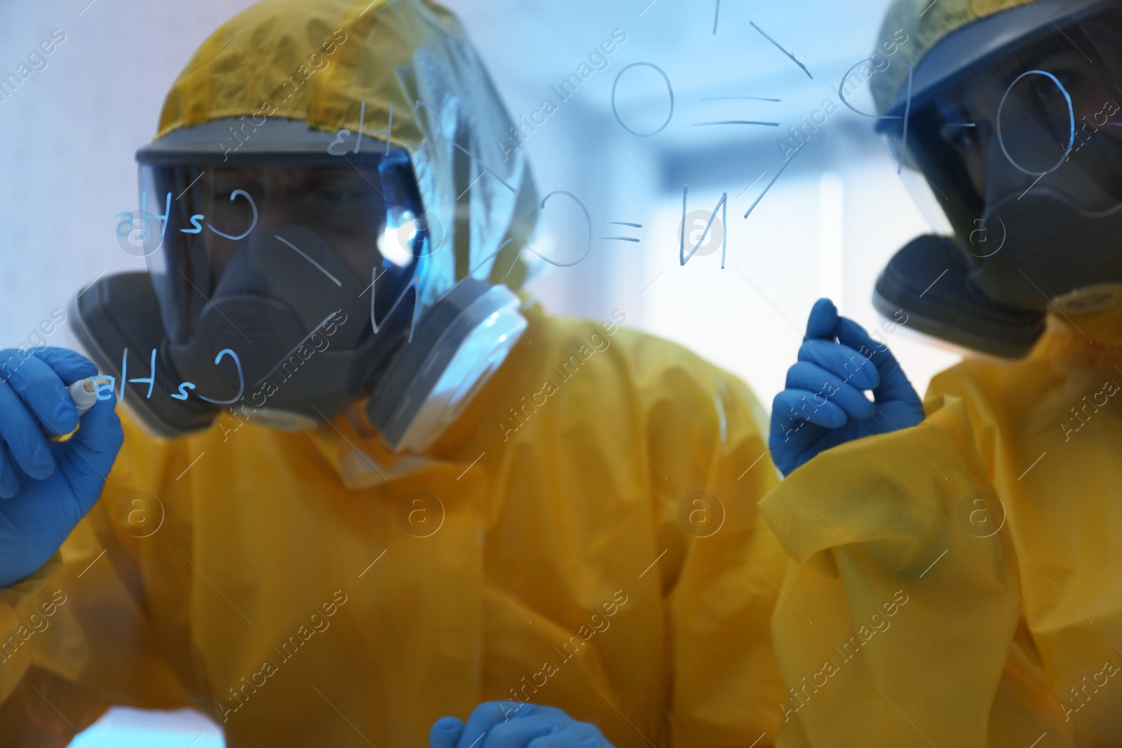 Photo of Scientists in chemical protective suits writing formula on glass board at laboratory. Virus research