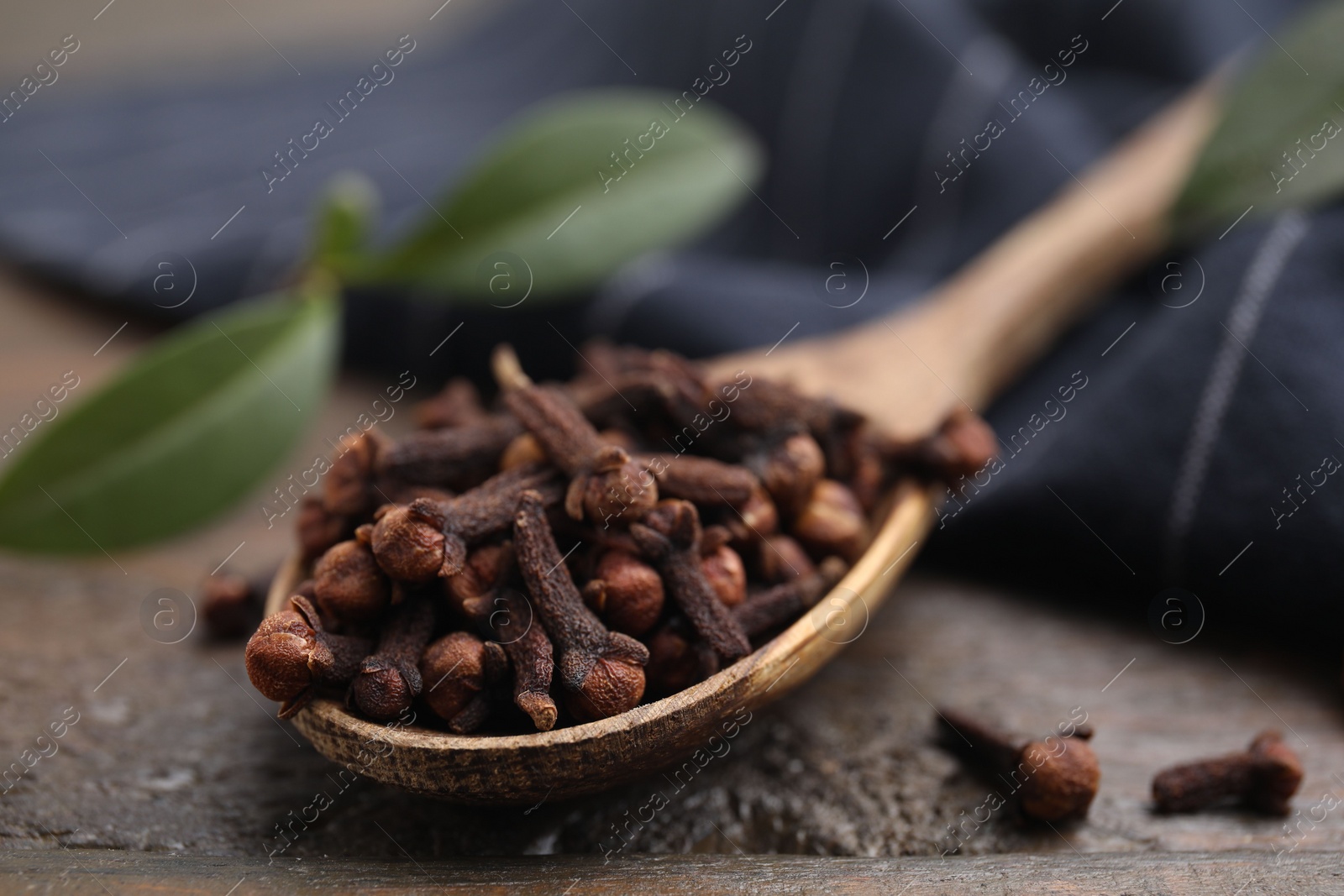 Photo of Spoon with aromatic cloves on wooden table, closeup