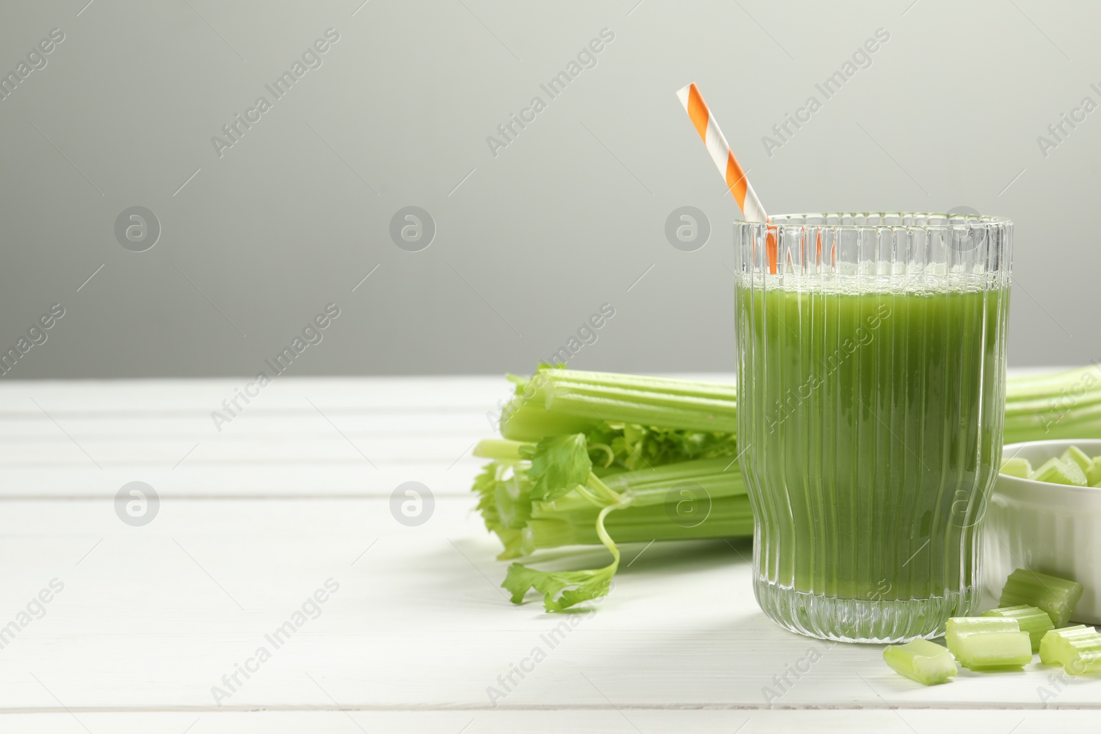 Photo of Glass of celery juice and fresh vegetables on white wooden table, space for text