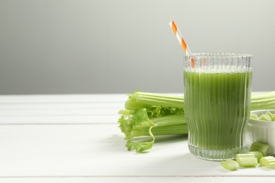 Glass of celery juice and fresh vegetables on white wooden table, space for text