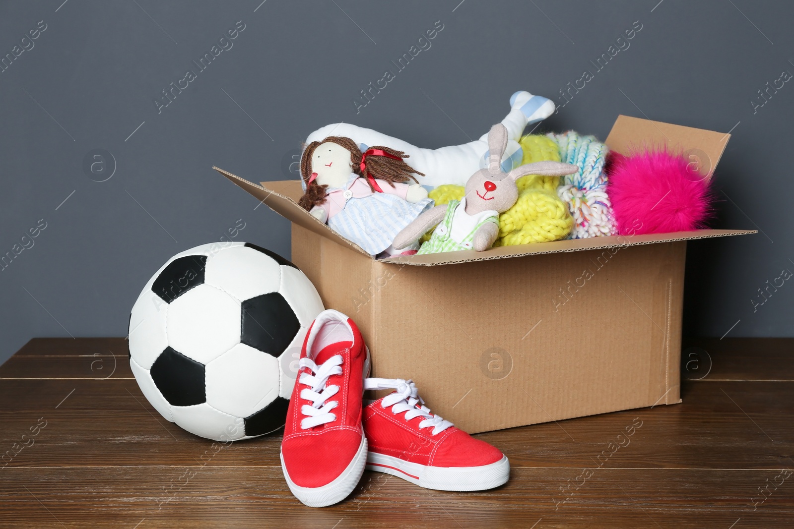 Photo of Donation box, shoes, toys and clothes on table near grey wall