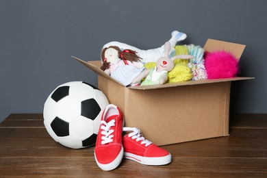 Photo of Donation box, shoes, toys and clothes on table near grey wall