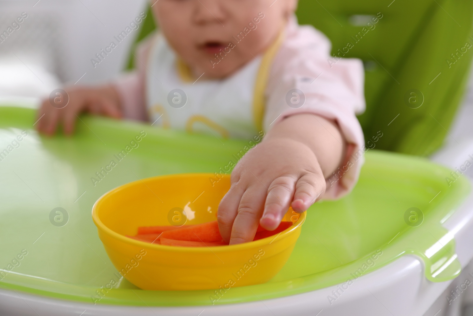 Photo of Little baby eating food in high chair at home, closeup