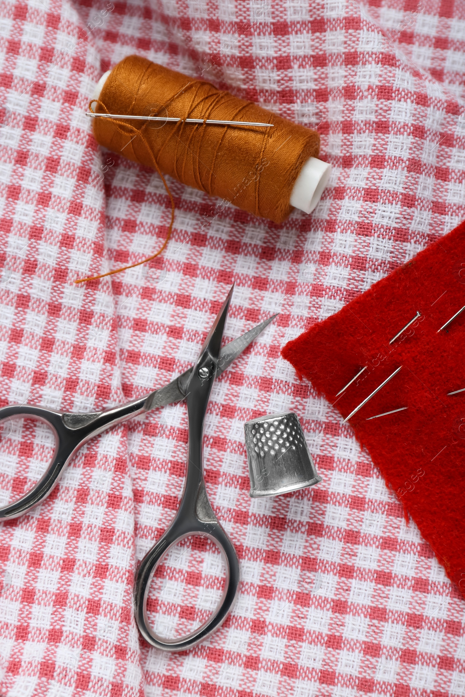 Photo of Flat lay composition with thimble and different sewing tools on checkered fabric