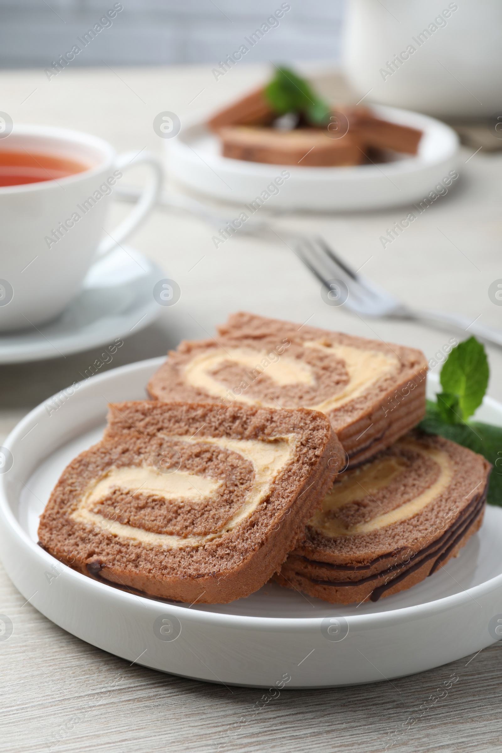 Photo of Tasty chocolate cake roll with cream and mint on light wooden table