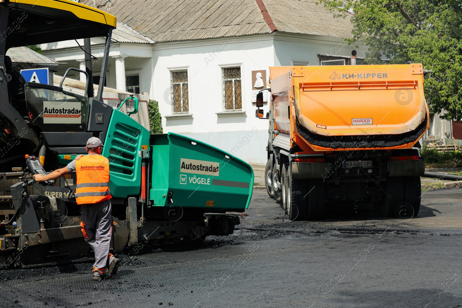 Photo of MYKOLAIV, UKRAINE - AUGUST 04, 2021: Worker with road repair machinery laying new asphalt