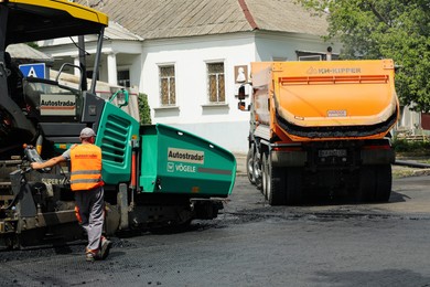 Photo of MYKOLAIV, UKRAINE - AUGUST 04, 2021: Worker with road repair machinery laying new asphalt