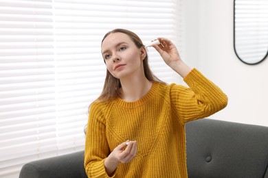 Photo of Young woman applying medical ear drops indoors