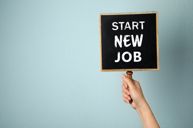 Image of Change your life. Woman holding blackboard with text Start New Job on light blue background, closeup. Space for text