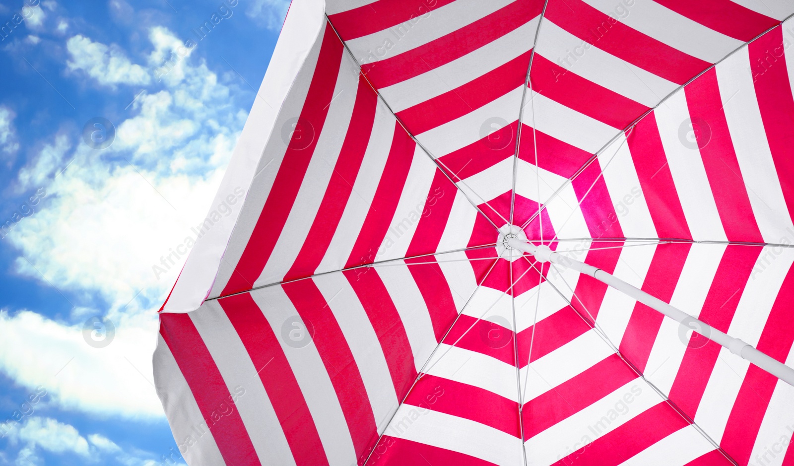 Image of Open big striped beach umbrella and beautiful blue sky with white clouds on background