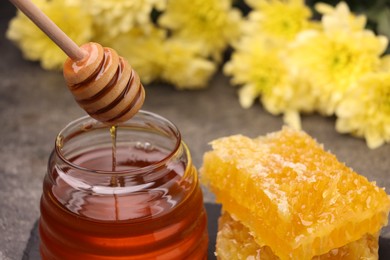 Photo of Pouring sweet golden honey from dipper into jar and pieces of honeycomb on table, closeup