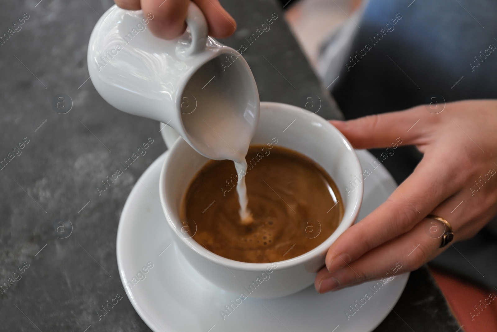 Photo of Woman adding milk to fresh aromatic coffee at table, closeup