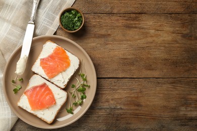 Delicious sandwiches with cream cheese and salmon on wooden table, flat lay. Space for text