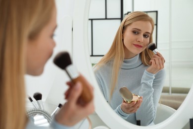 Beautiful woman applying makeup near mirror in room