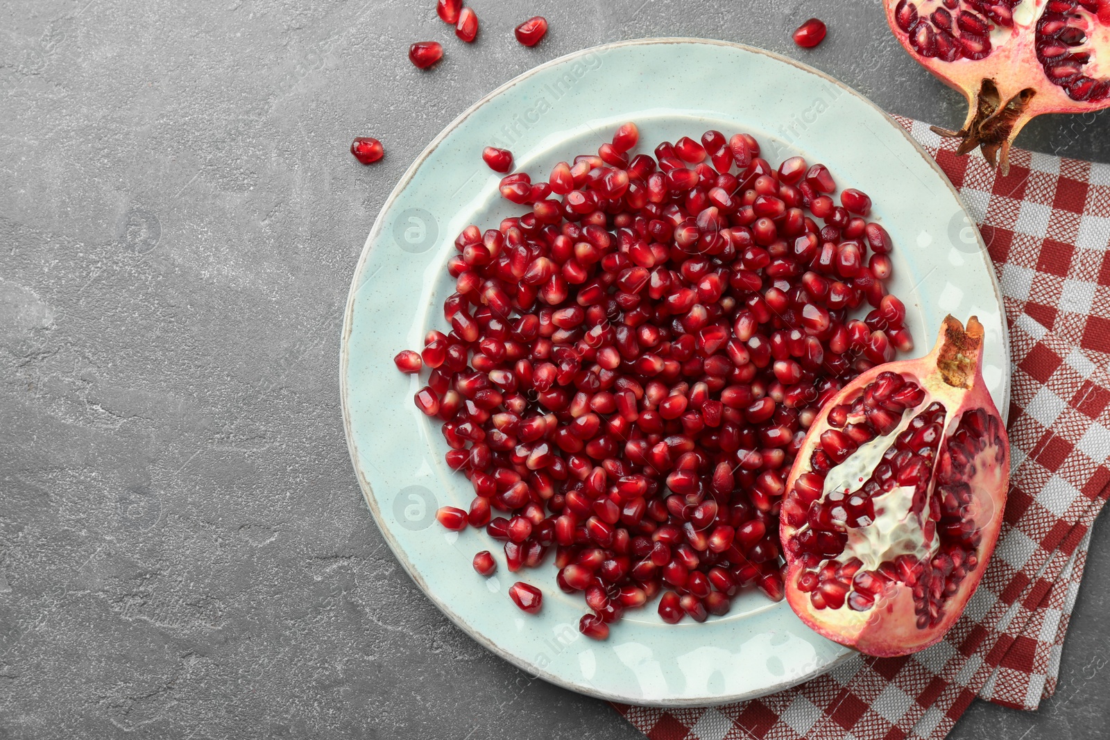 Photo of Tasty ripe pomegranate and grains on grey table, flat lay. Space for text