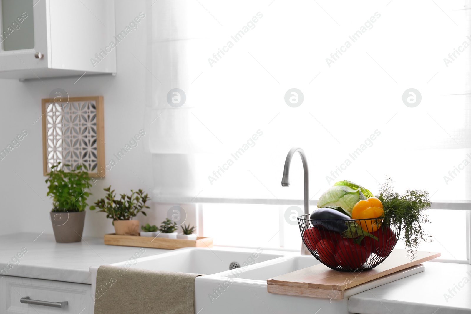 Photo of Basket full of different vegetables on wooden board in modern kitchen