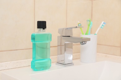 Photo of Mouthwash and holder with toothbrushes on sink in bathroom. Teeth and oral care